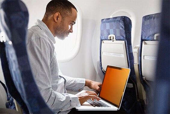 En man som arbetar på ett flygplan med en bärbar dator med ett guldfärgat sekretessfilter