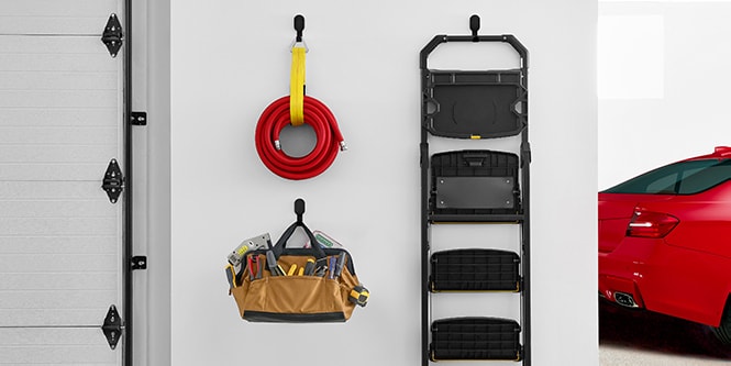 En vägg i ett garage med 3M CLAW™ krok för gipsskiva med slang, stege och campingstol.
