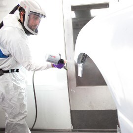 Lackerare sprayar en vit bilkarossdel med hjälp av 3M-spraysystem