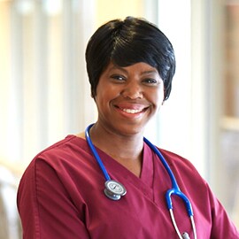 Leende sköterska i vinröda arbetskläder med ett 3M Littmann Classic III stetoskop med blå slangar.
