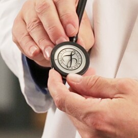 Närbild på en läkare som håller bröststycket på ett 3M Littmann stetoskop med Littmann-märket på membranet.