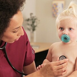Pediatriksjuksköterska som lyssnar på bröstet hos ett litet barn med ett 3M Littmann Classic III stetoskop.