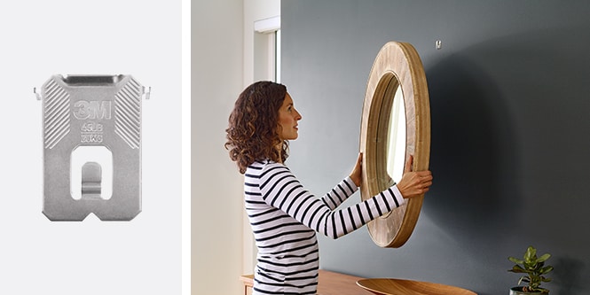 Kvinna som hänger rund träspegel på en mörk vägg och använder 3M CLAW™ Tavelhängare för gipsvägg
