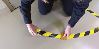 En bild som innehåller personen som klibbar gul-svart tejp på golvet
