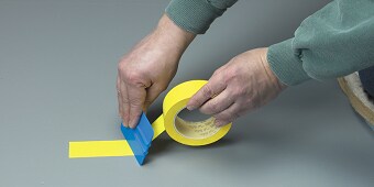 En bild som innehåller personen som klibbar gul tejp på golvet
