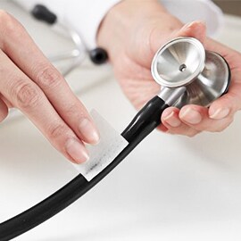 Händer som torkar av slangen på ett Littmann stetoskop med en spritduk.