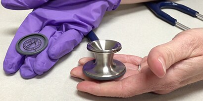 Händer som håller i ett 3M™ Littmann® Classic III™ Stetoskopbröststycke och avtagbart membran.

