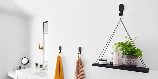 En vägg i ett badrum med 3M CLAW™ krok för gipsskiva med hängande växt och handdukar.
