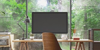 Bildskärm på ett skrivbord, med en skog synlig i bakgrunden
