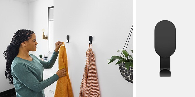  Kvinna hänger handdukar på svarta väggkrokar från 3M CLAW™ i badrummet
